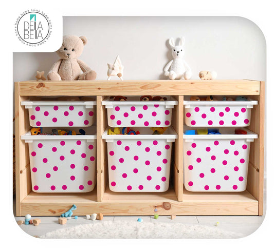 A light natural wood children's storage cabinet with six white plastic bins decorated with bright pink polka dots, styled with toys and plush toys on top against a white wall.