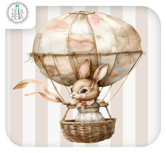 A watercolor-style illustration of a small rabbit in a wicker basket attached to a pastel hot air balloon, set against a cream and beige striped background. A circular Della Bella brand mark appears in the top-left corner.